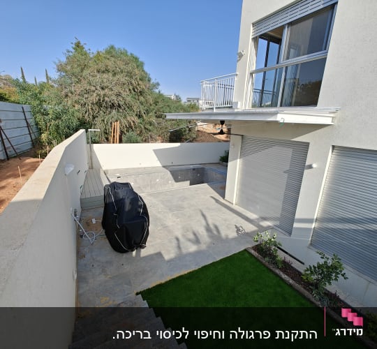 חצר עם דשא סינתטי וצמחייה לצד קיר בטון